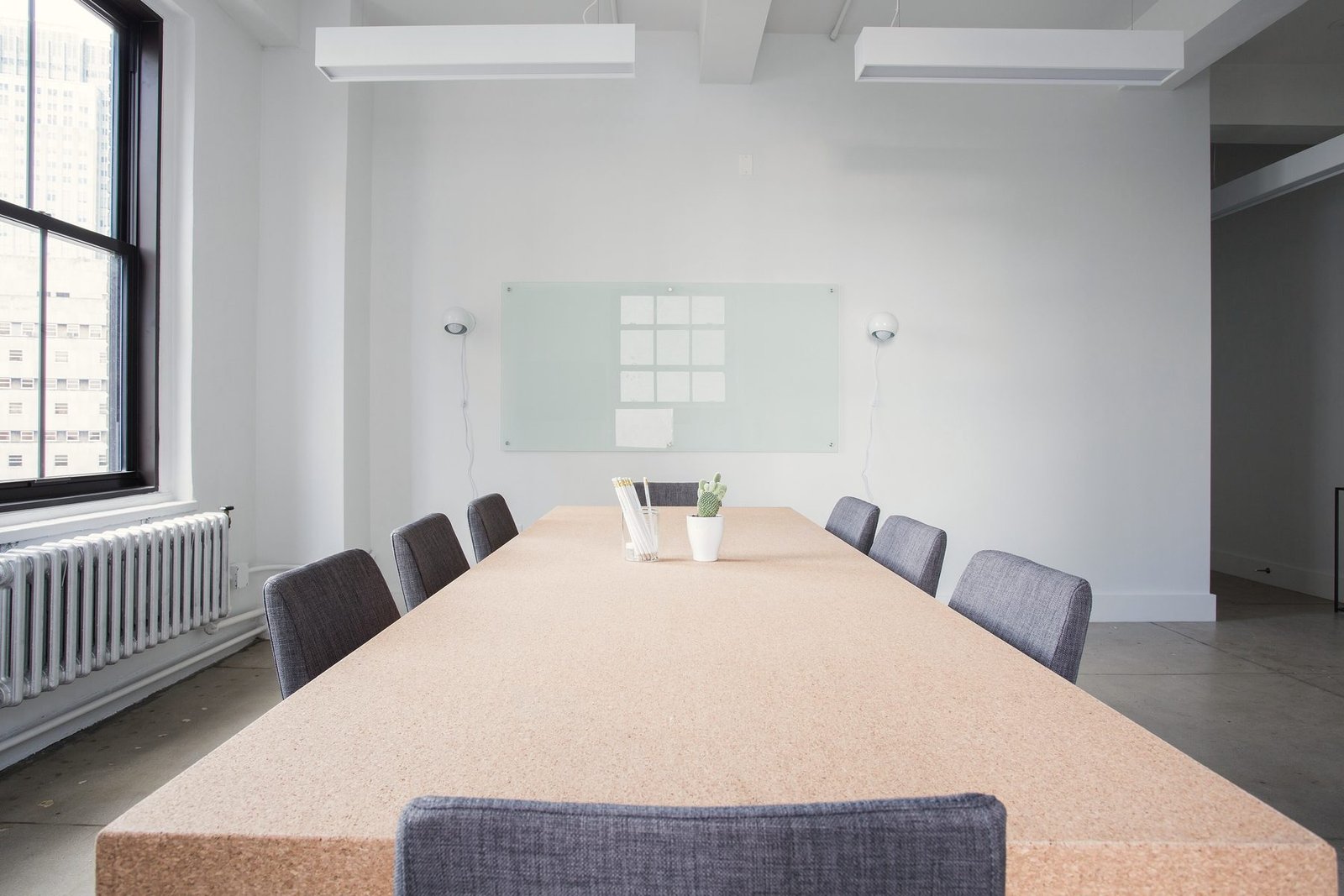 A cork-topped conference table with chairs beside tall windows