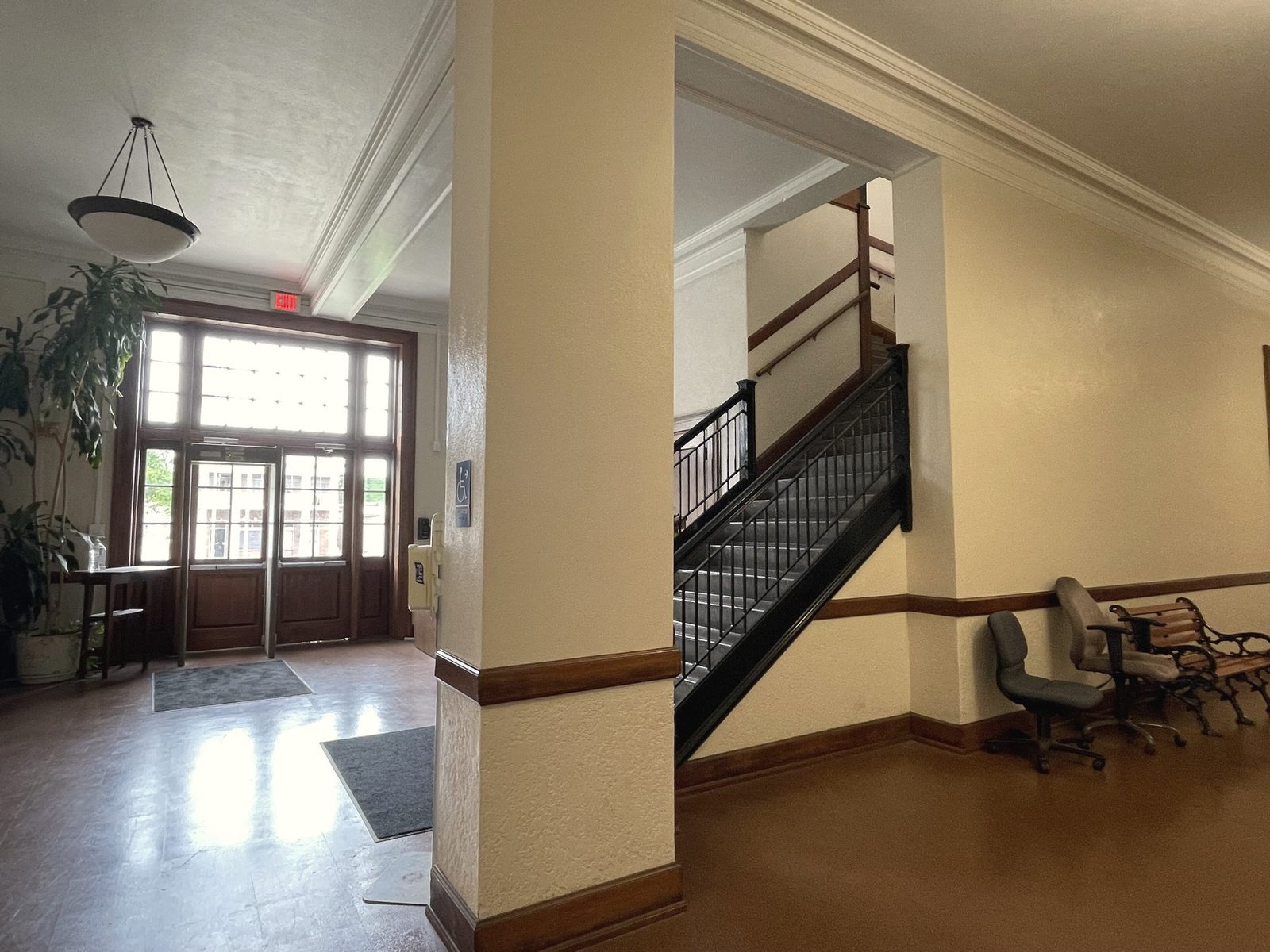 A courthouse hallway with a staircase, wooden doors and benches